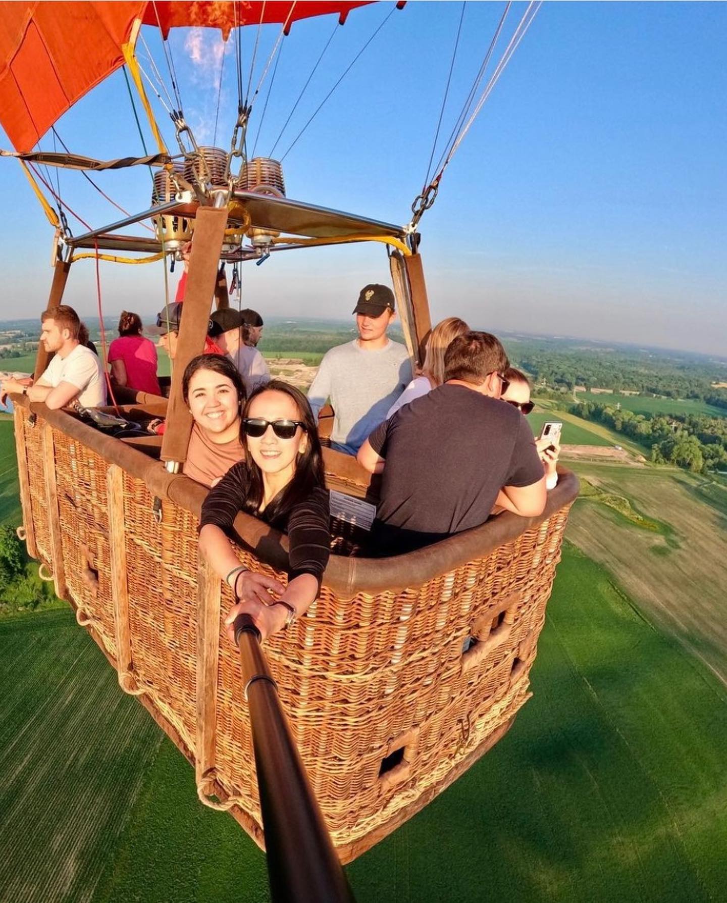 Friends from Oakville taking a selfie in the hot air balloon basket above green fields